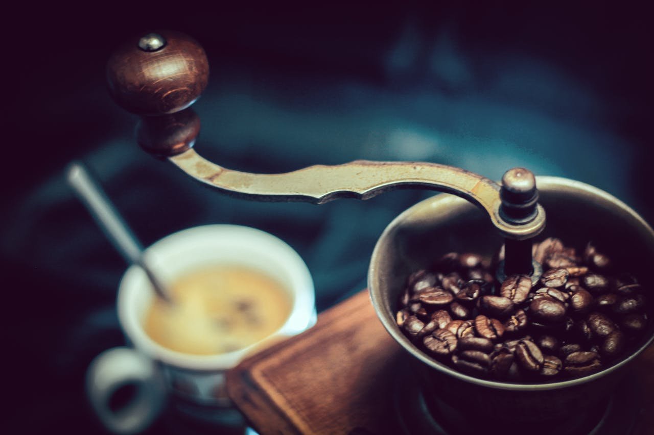 Close-up of a vintage coffee grinder with fresh coffee beans next to a steaming cup.